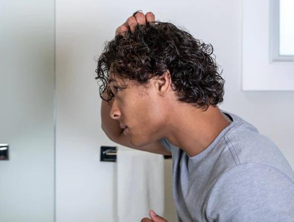 A man checking for  seasonal hair loss in the mirror